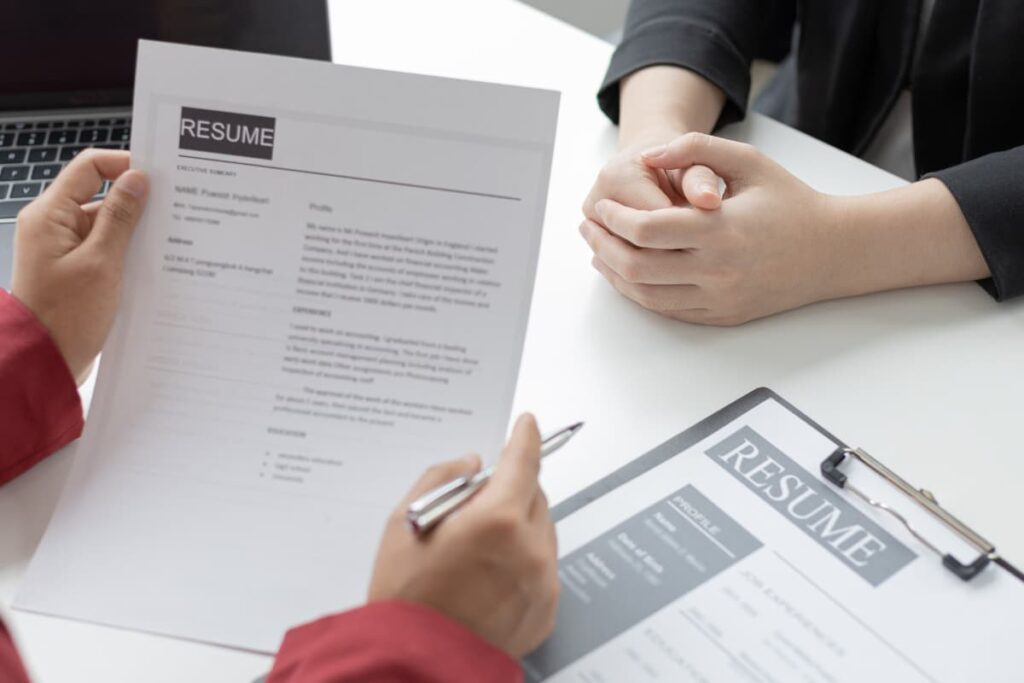 Starbucks Interviews employees, employees carries resume to the interview. On a table there is a resume attached with the pad, interviewer holds a resume and pen on his/her right hand and interviews to the another person.