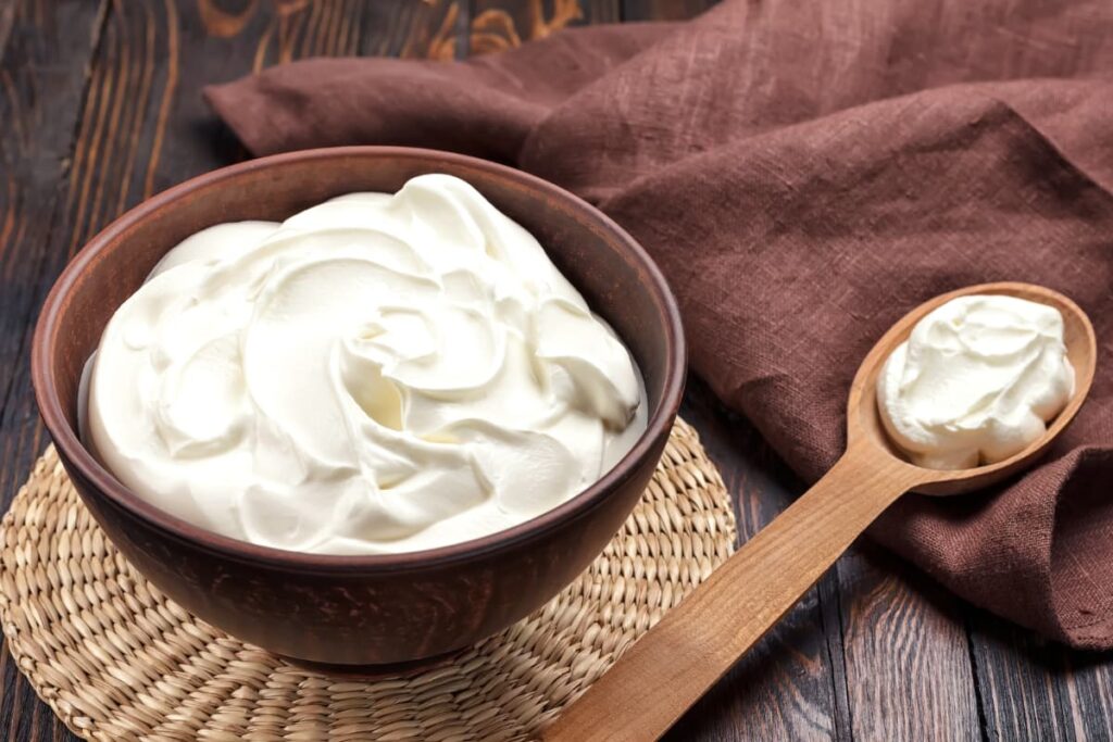 Starbucks Heavy Cream can be served in a maroon red color bowl, and a spoon of heavy cream besides to the bowl. This bowl, spoon is kept on a brown color table, along with the maroon red color cloth and a handmade plate is under the bowl.